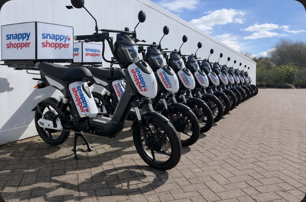 Row of electric scooters with 'Snappy Shopper' branding parked in front of a building.