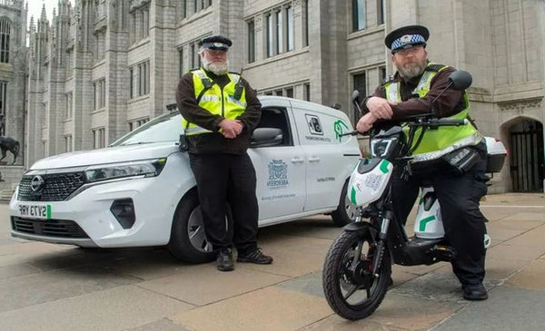 Two police officers standing with a motorcycle and a white van in front of a building.