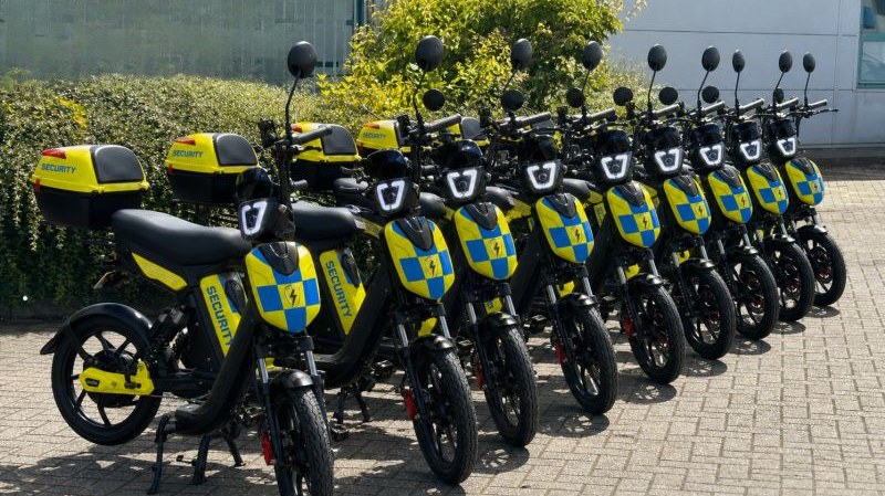 Ten Eskuta SX-250s in Battenburg security livery lined up outside a commercial building, each with a branded top box